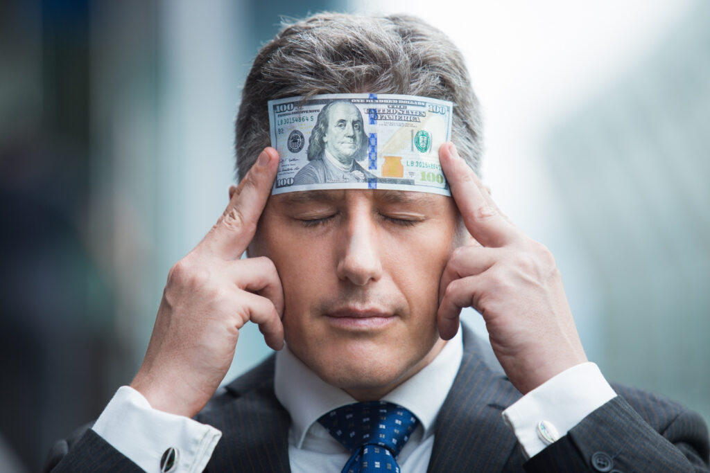 Man in a business suit concentrating with a $100 bill placed on his forehead, symbolizing money mindset and financial focus.